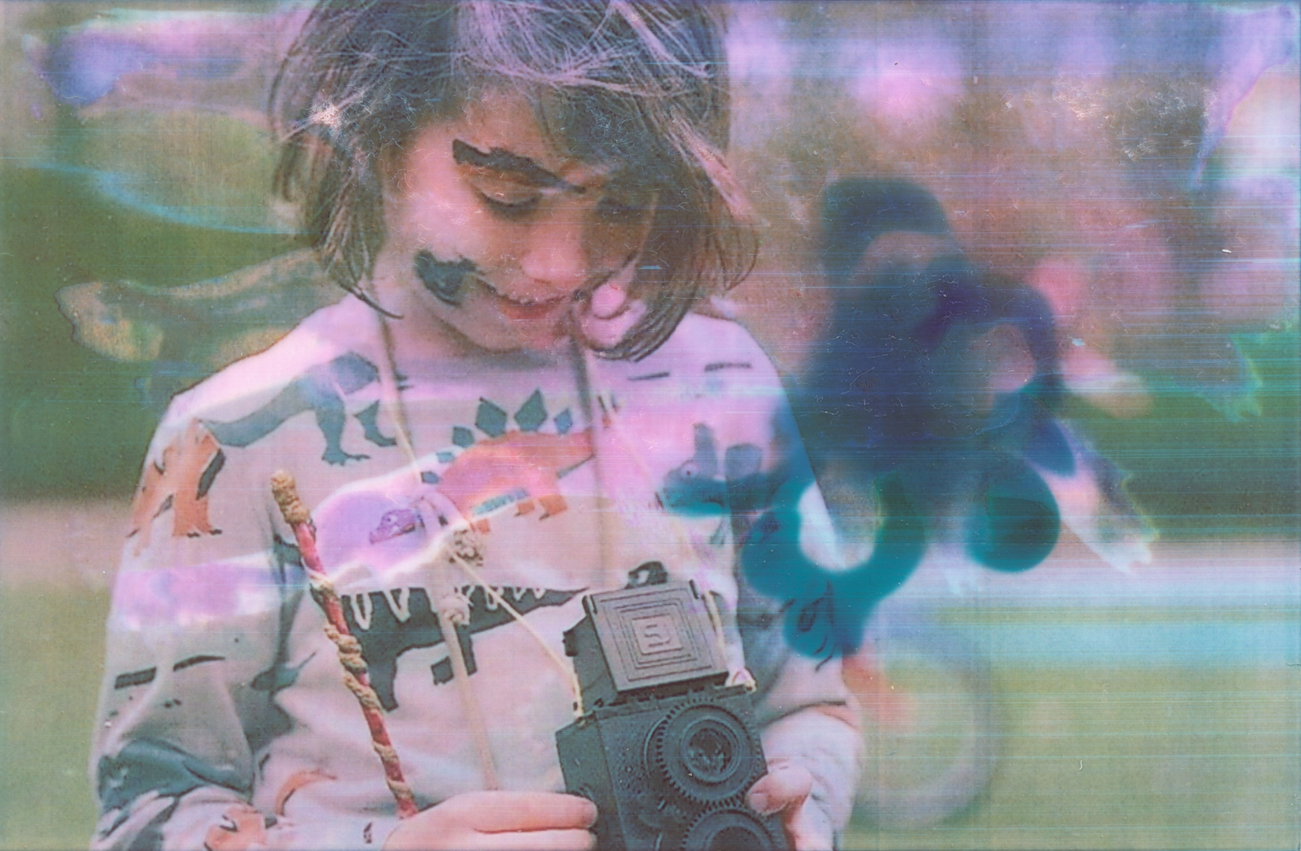 Ein farbiges Porträt eines Jungen mit experimentellen Farbfehlern auf Zink Fotopapier, der eine selbstgebaute zweiäugige Kamera in den Händen hält und fotografiert.
